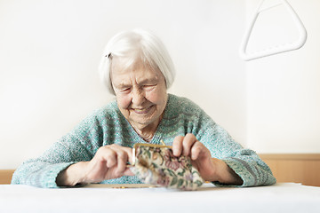 Image showing Cheerful elderly 96 years old woman sitting at table at home happy with her pension savings in her wallet after paying bills.