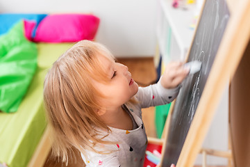 Image showing happy little girl drawing on chalk board at home