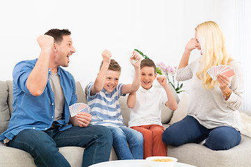 Image showing Happy family playing card game on living room sofa at home and having fun together celebrating the game winner