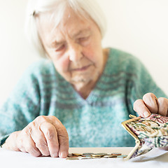 Image showing Concerned elderly woman sitting at the table counting money in her wallet.