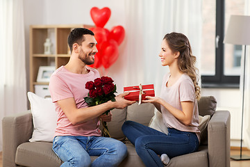 Image showing happy man giving woman flowers and present at home