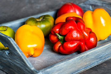 Image showing Imperfect natural peppers and tomatoes on an old wooden tray on a dark background. Healthy eating concept.