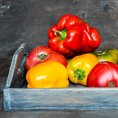 Image showing Imperfect natural peppers and tomatoes on an old wooden tray on a dark background. Healthy eating concept.