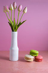 Image showing Macaroons on a pale pink background next to a vase of tulips. Place for text.