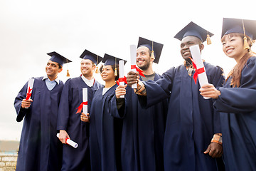 Image showing happy students in mortar boards with diplomas