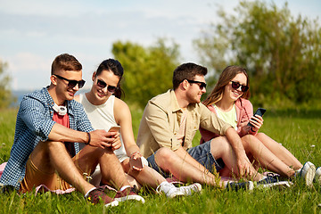 Image showing smiling friends with smartphones sitting on grass