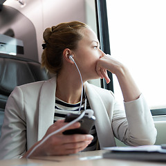 Image showing Thoughtful businesswoman listening to podcast on mobile phone while traveling by train.