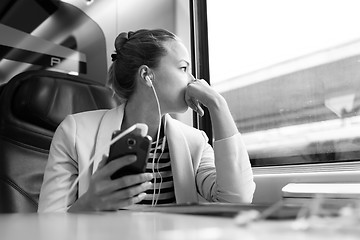 Image showing Thoughtful businesswoman listening to podcast on mobile phone while traveling by train.