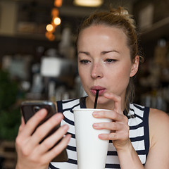 Image showing Thoughtful woman reading news on mobile phone while sipping coffee in coffee shop.