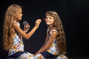 Image showing The older sister is applying powder to the younger girl\'s face