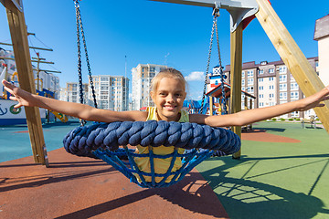 Image showing Girl joyfully spread her arms while riding on a round hanging swing