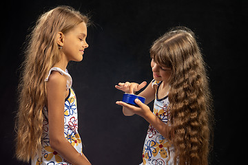 Image showing A girl puts jar cream on her finger, another girl sits nearby