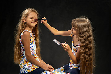 Image showing The girl closed her eyes when another girl powder her nose with a brush