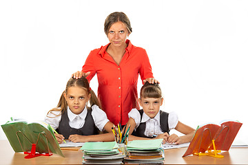 Image showing Angry teacher stands behind students sitting at her desk and puts her hands on the heads of children