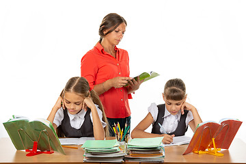 Image showing Schoolchildren at the desk do the assignment, the teacher in the background reads the assignment