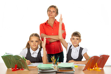 Image showing Children pull their hands up, ready to answer a question, in the background a satisfied teacher