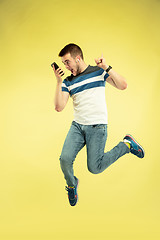 Image showing Full length portrait of happy jumping man with gadgets on yellow background