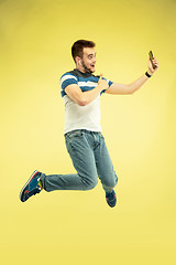 Image showing Full length portrait of happy jumping man with gadgets on yellow background