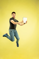 Image showing Full length portrait of happy jumping man with gadgets on yellow background