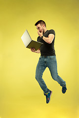 Image showing Full length portrait of happy jumping man with gadgets on yellow background