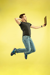 Image showing Full length portrait of happy jumping man with gadgets on yellow background