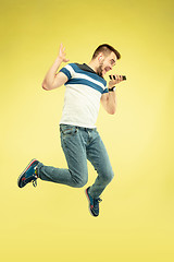 Image showing Full length portrait of happy jumping man with gadgets on yellow background