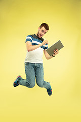 Image showing Full length portrait of happy jumping man with gadgets on yellow background