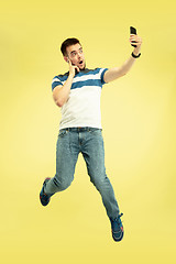 Image showing Full length portrait of happy jumping man with gadgets on yellow background