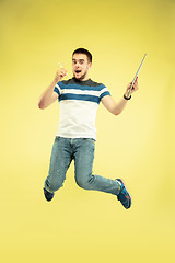 Image showing Full length portrait of happy jumping man with gadgets on yellow background