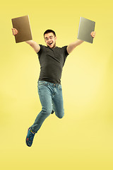 Image showing Full length portrait of happy jumping man with gadgets on yellow background