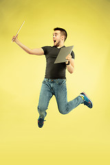 Image showing Full length portrait of happy jumping man with gadgets on yellow background