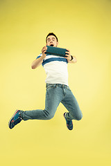 Image showing Full length portrait of happy jumping man with gadgets on yellow background