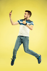 Image showing Full length portrait of happy jumping man with gadgets on yellow background