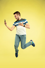 Image showing Full length portrait of happy jumping man with gadgets on yellow background