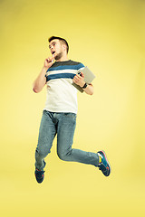 Image showing Full length portrait of happy jumping man with gadgets on yellow background