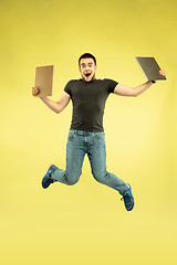 Image showing Full length portrait of happy jumping man with gadgets on yellow background