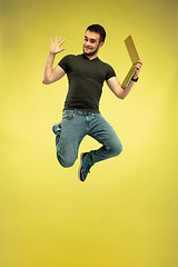 Image showing Full length portrait of happy jumping man with gadgets on yellow background