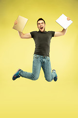 Image showing Full length portrait of happy jumping man with gadgets on yellow background