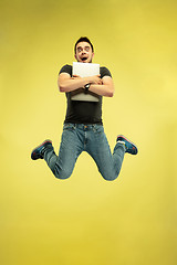 Image showing Full length portrait of happy jumping man with gadgets on yellow background