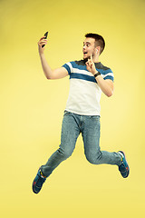 Image showing Full length portrait of happy jumping man with gadgets on yellow background