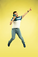 Image showing Full length portrait of happy jumping man with gadgets on yellow background