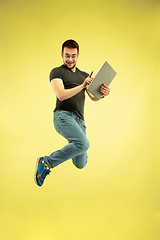 Image showing Full length portrait of happy jumping man with gadgets on yellow background