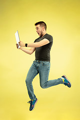 Image showing Full length portrait of happy jumping man with gadgets on yellow background