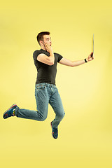 Image showing Full length portrait of happy jumping man with gadgets on yellow background