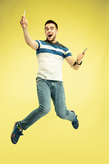 Image showing Full length portrait of happy jumping man with gadgets on yellow background