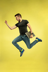 Image showing Full length portrait of happy jumping man with gadgets on yellow background