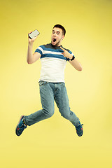 Image showing Full length portrait of happy jumping man with gadgets on yellow background