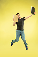 Image showing Full length portrait of happy jumping man with gadgets on yellow background