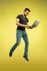 Image showing Full length portrait of happy jumping man with gadgets on yellow background