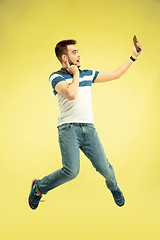 Image showing Full length portrait of happy jumping man with gadgets on yellow background